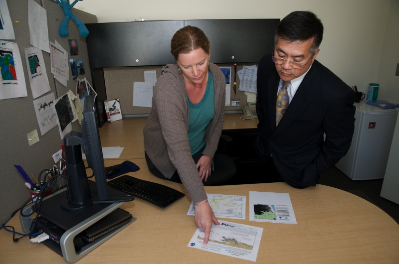 A woman in an office pointing to a piece of paper as she talks to a man. 