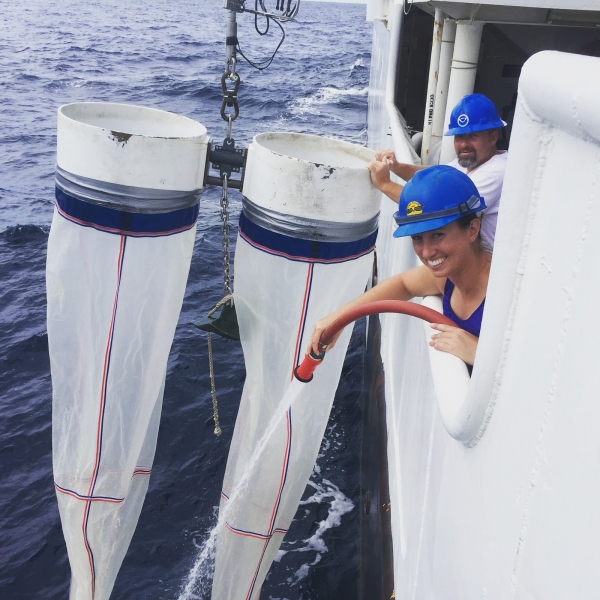 A woman leans over the side of the boat with a large hose, spraying down a long, white mesh net.