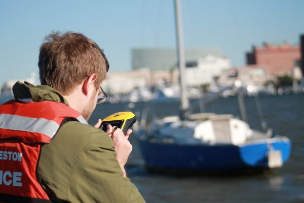 A person holding a device with a derelict vessel in the background. 