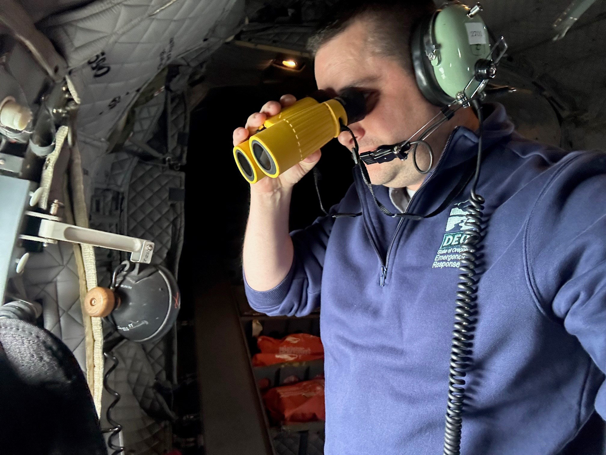 Man uses binoculars from an airplane.