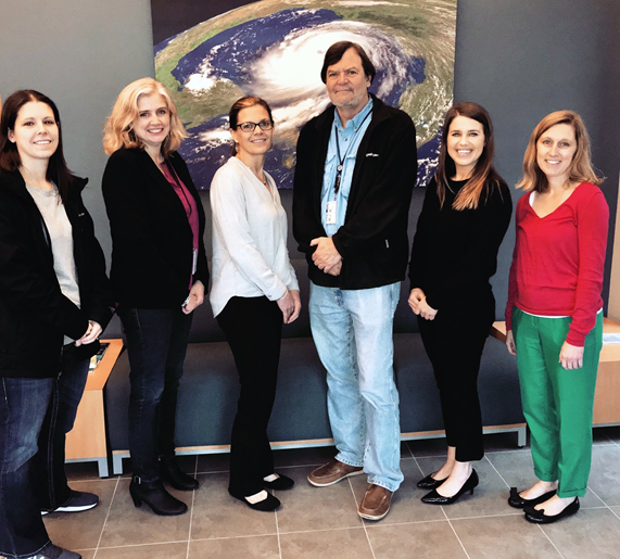 Six people standing in front of a satellite photo of a hurricane.