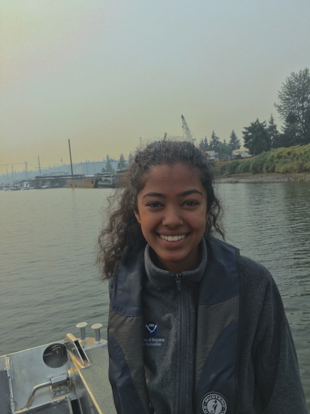 A photo of a girl on a boat with an industrial shoreline in the background.