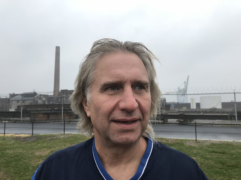 A profile shot of a man with an industrial setting in the background. 