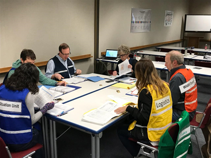 A group of people in different colored vests sitting at a table. 