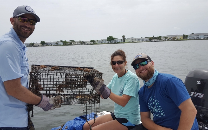 Three people holding up a crab cage.