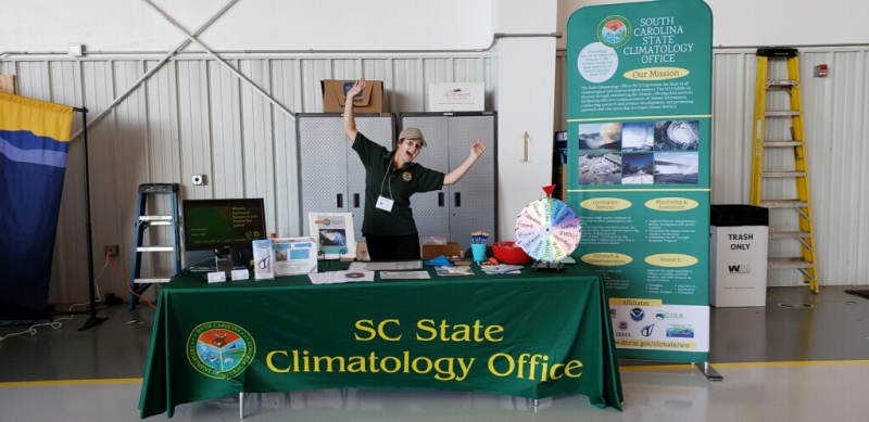 A girl posing for a photo at a table with a "SC State Climatology Office" banner.