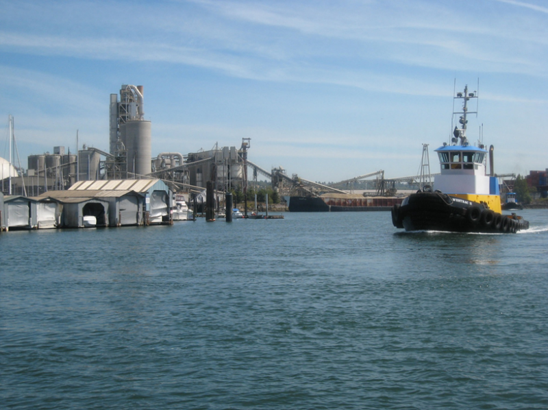 A boat on a river with an industrial shoreline to the left.