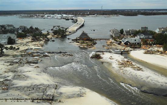 A collapsed bridge with water pouring through a strip of land.