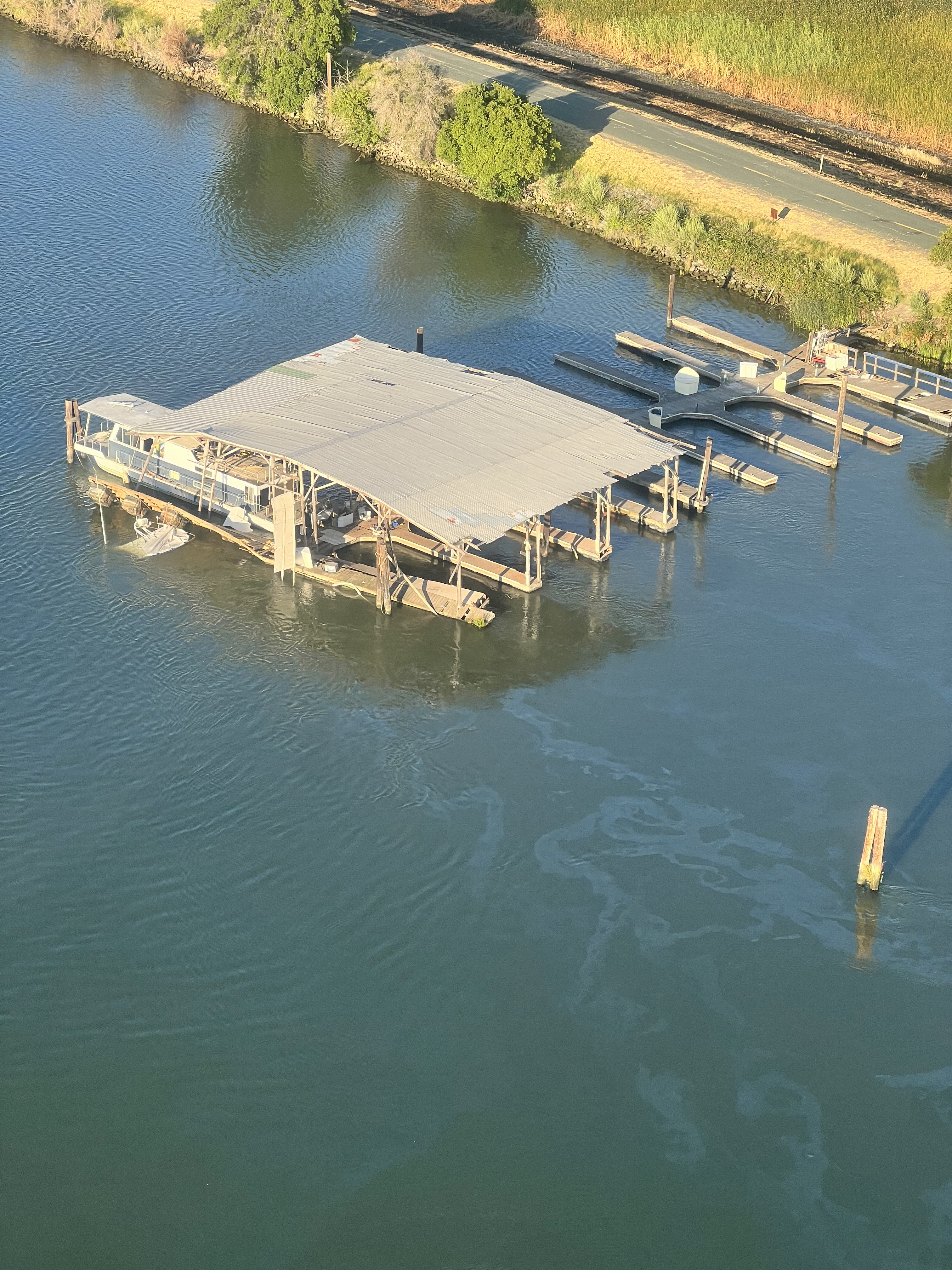 Aerial view of sheen near a marina at Threemile Slough, California, July. 3, 2024. A partially exposed sunken vessel can be seen on the waterward side of the covered finger piers.