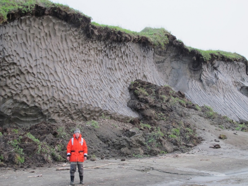 A woman with a wall of exposed permafrost behind her.
