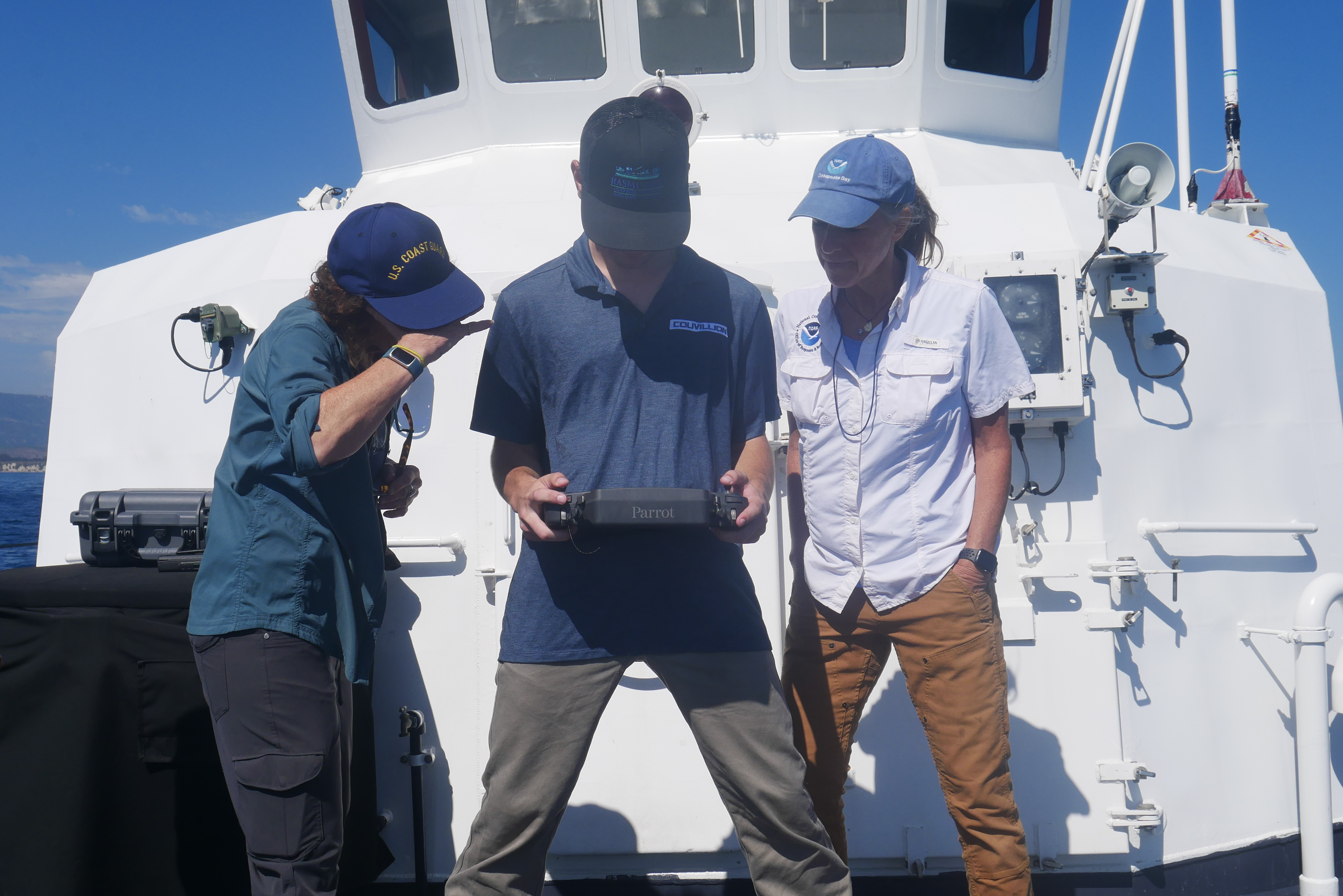 Project team members aboard a response vessel, observing a UAS pilot's flight within its remote controller's screen.