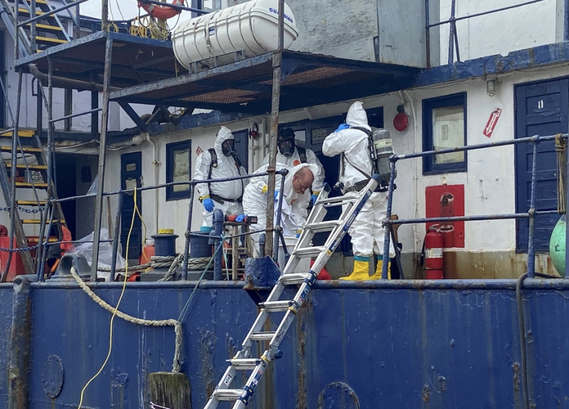 Response workers in white hazmat suits work on the deck of a fishing vessel.