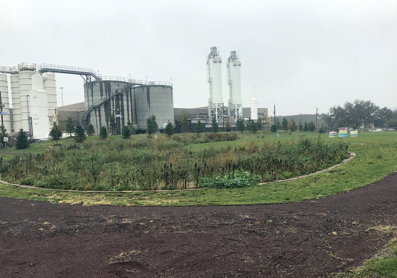 A grassy park with industrial structures in the background. 