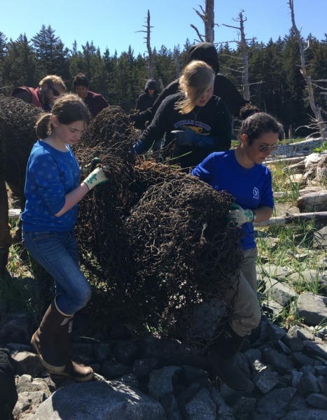 A group of people hauling a large block of fish netting and other debris.