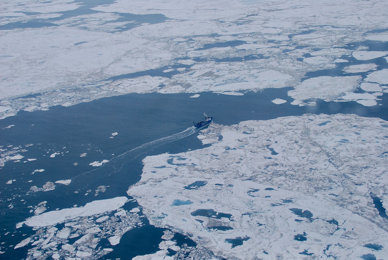 An aerial view of a research vessel transiting through sea ice.