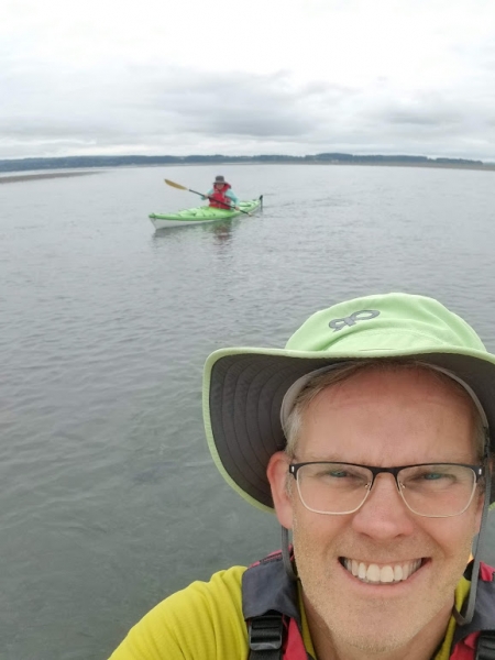 A person taking a selfie in a kayak with another kayaker in the background.