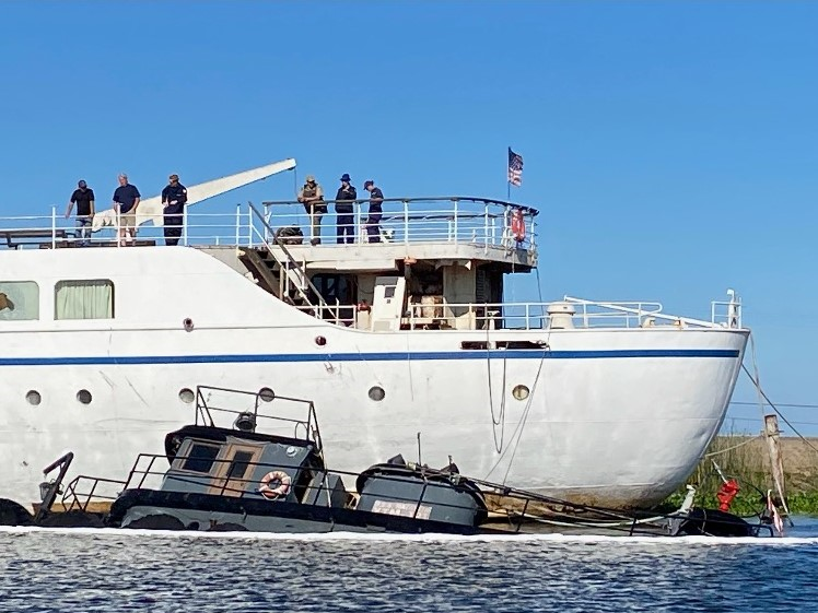 A tug partially sunk in a river near a much larger vintage vessel in the background.