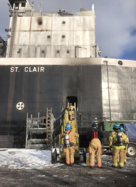 A group of firefighters ascending the stairs to a vessel with the name "St. Clair" on the side. 
