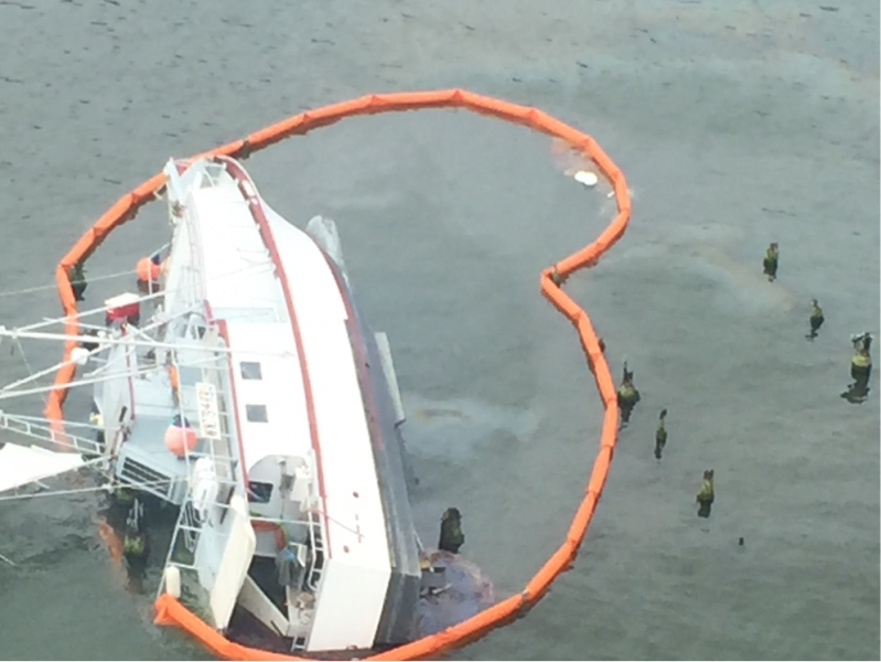 A vessel capsized on its side surrounded by pollution boom.