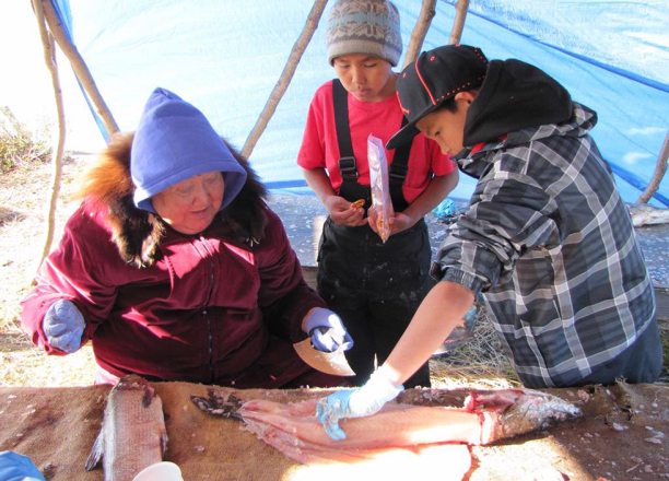 A woman and two children cut a pike for drying. 