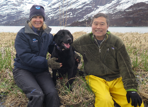 A man, a woman, and a dog with a mountain in the background. 
