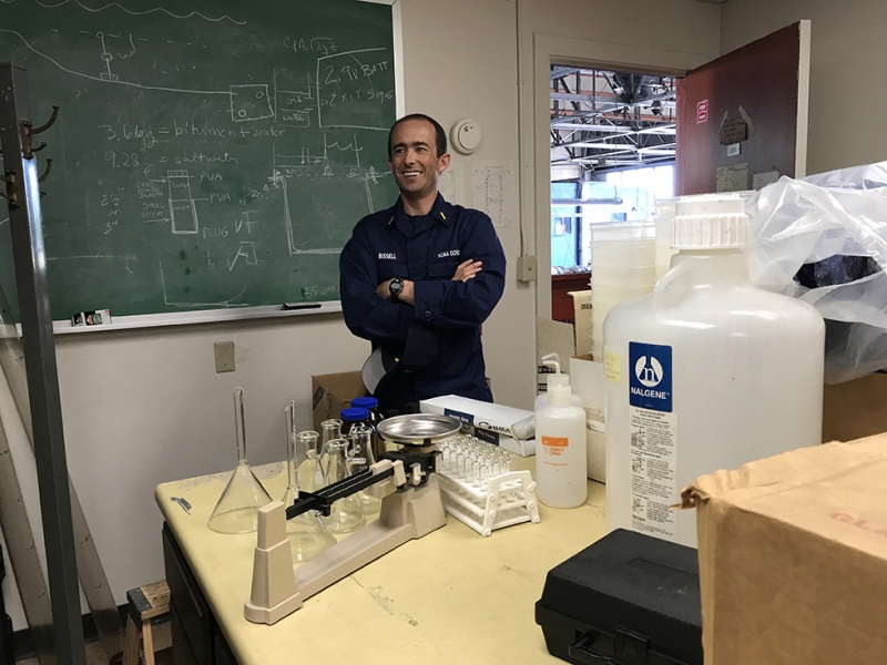 A man standing in a lab with a chalkboard in the background. 