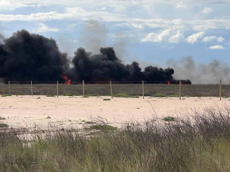 Thick black smoke rising over a field in the distance.