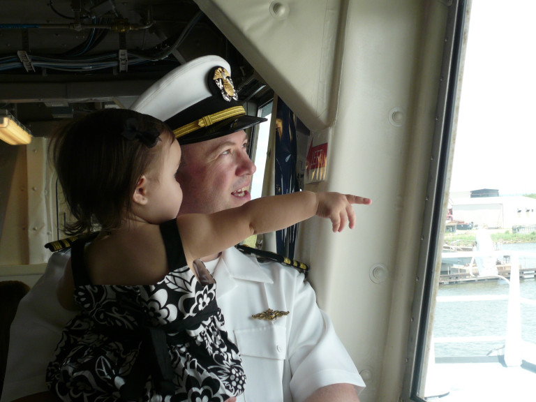 A man in uniform holding a little girl as they look out the window of a vessel. 