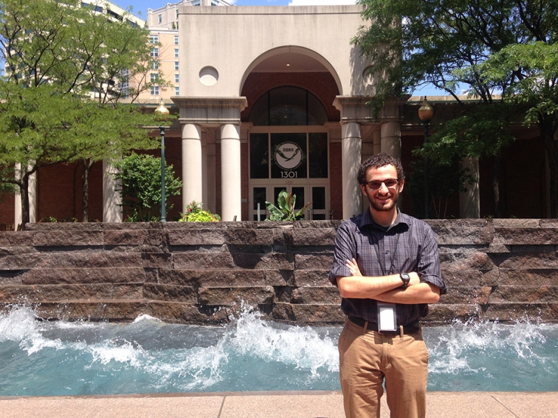 A man standing in front of a wave pool with a NOAA building in the background. 