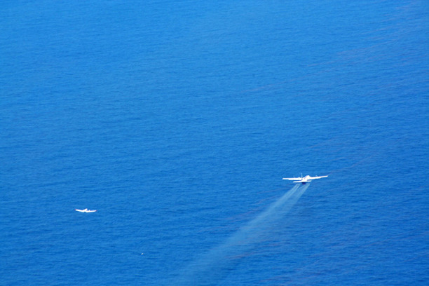 A plane flying over water with a trail of dispersant following.