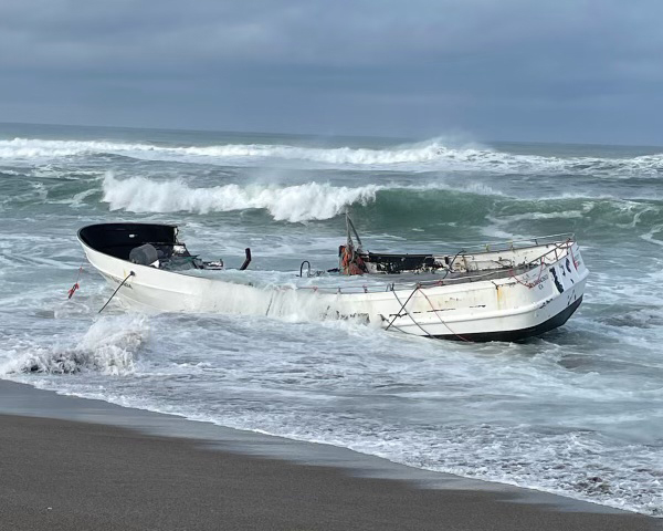 A fishing vessel grounded on a sandy beach in a degraded state.