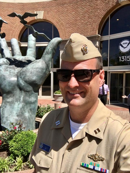 A man in military uniform standing in front of a statue of a hand. 