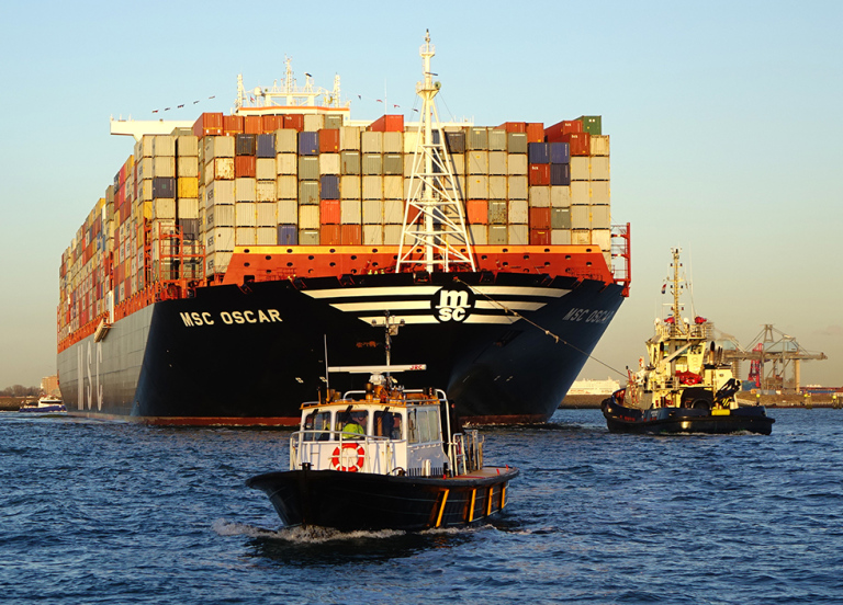A small boat in the foreground with a massive container ship in the background.