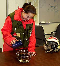 A person pouring a substance into a glass bowl filled with a clear liquid and black spots in it.