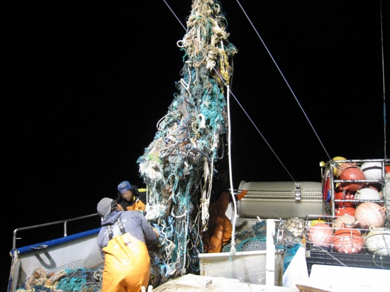 A large tangle of fishing nets being hoisted onto a boat. 