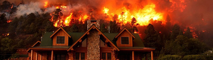 A house with a mountainside on fire behind it. 