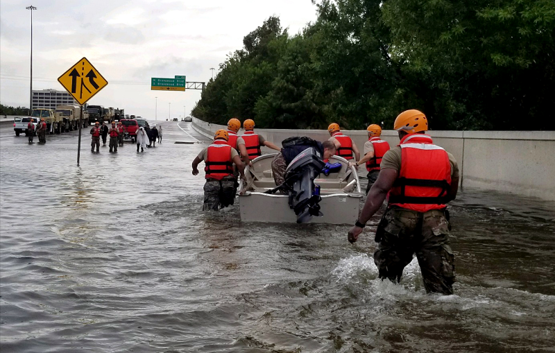 A group of people walking through a flooded highway with a boat.