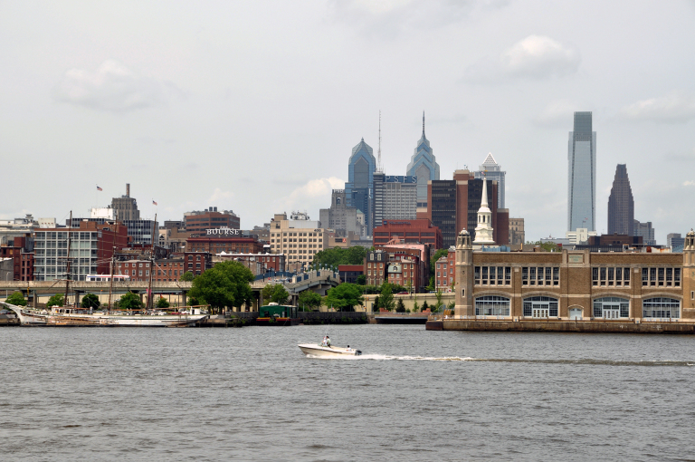 A boat crossing a body of water with a cityscape in the background. 