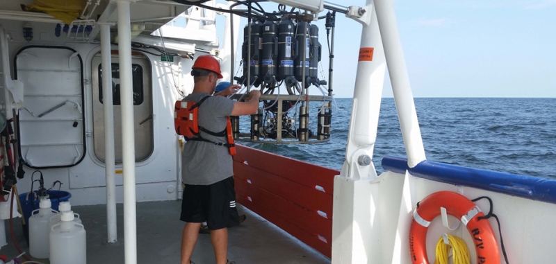 A man standing on a boat operating a large piece of machinery that is being placed into the water. 