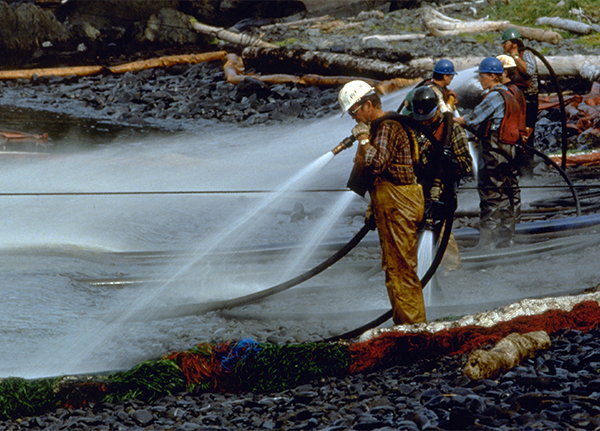 Workers spraying a rocky shoreline with high-pressure water. 