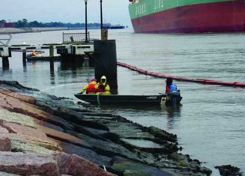 People on a boat pressure washing a shore.