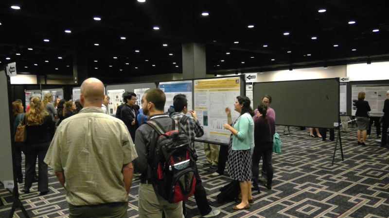 A large group of people standing around talking inside a conference space. 