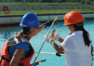 Two people in hard hats looking at an item on the end of a long metal pole. 