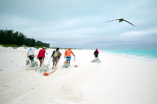 A group of people drag derelict nets across a sandy beach in the Papahānaumokuākea Marine National Monument.