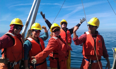 A group of people wearing hard hats and life vests on a boat. 