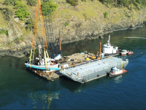 A crane secured on a barge lifts a sunken vessel onto the barge.