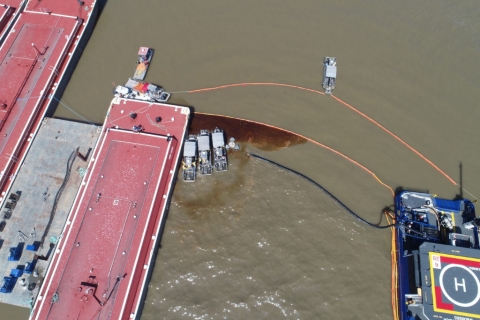 An aerial image of a several vessels with oil caught in pollution boom between the vessels.