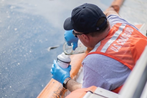 A man in a U.S. Coast Guard vest pouring oiled water into a container.