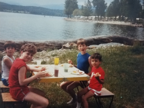 Four kids at a picnic table by a lake.