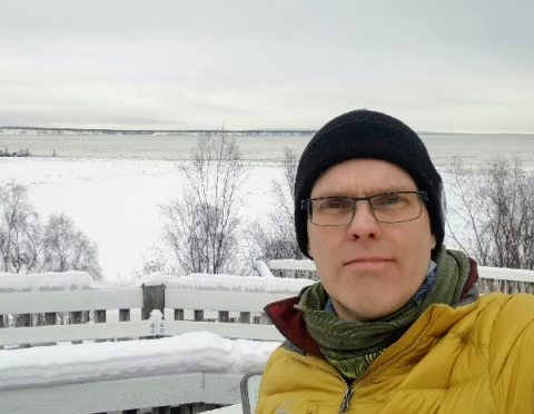 A man posing for a photo in front of a wintery landscape. 
